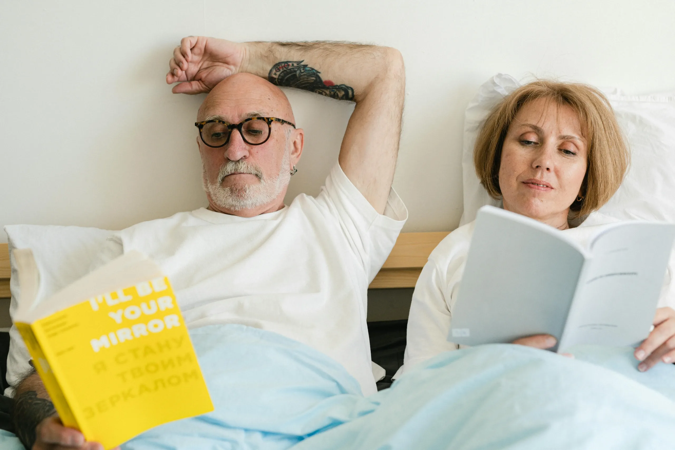 Older couple lying in bed reading books